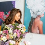 A girl with a bouquet of flowers against the background of a modern painting hanging on the wall