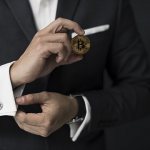 A man in a suit holds a bitcoin in his hand
